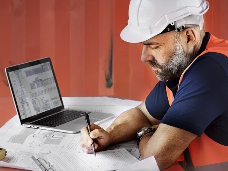 Un homme en tenue de chantier étudie sur son bureau des documents pour faire un DICT