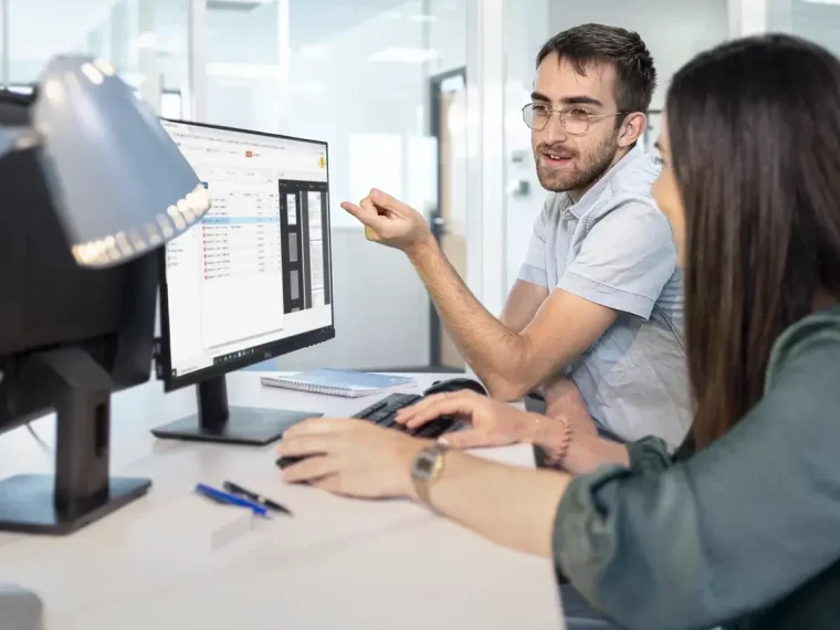Deux collègues qui échangent sur un bureau avec un ordinateur