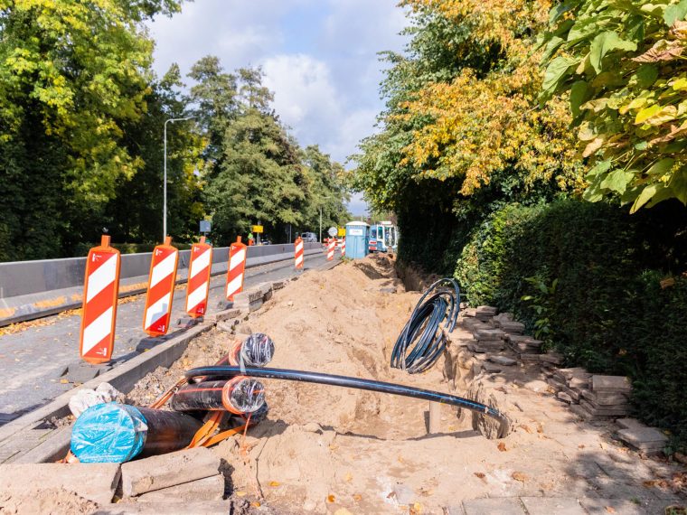 Open sleuf langs een weg met kabels en leidingen, afzetbakens en opgestapelde stoeptegels