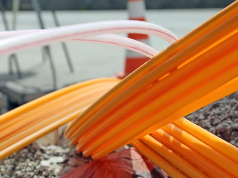 Bundels oranje en wit-rode kabelbuizen naast een sleuf, met een pylon en dranghekken op de achtergrond