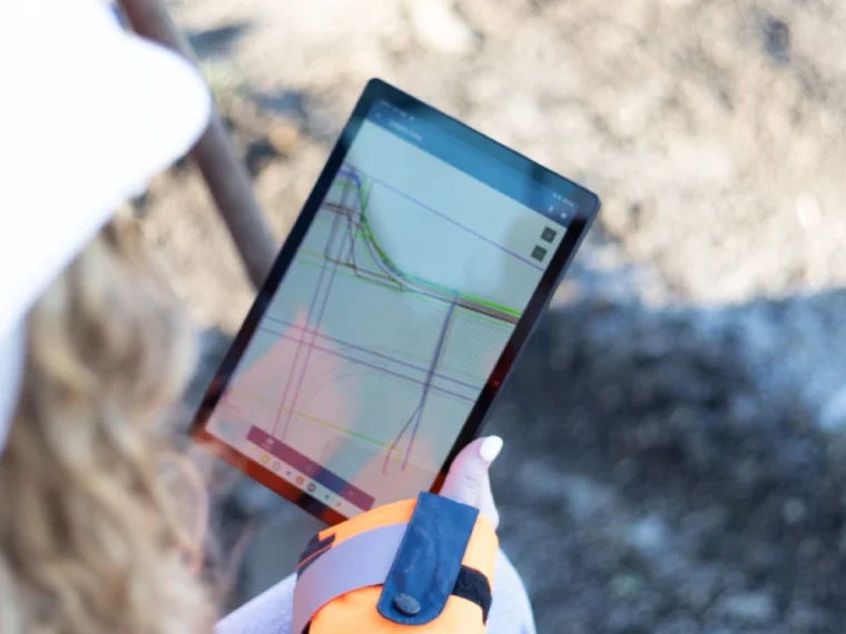 Medewerker met helm houdt in het veld een tablet vast met een digitale tekening van kabels en leidingen