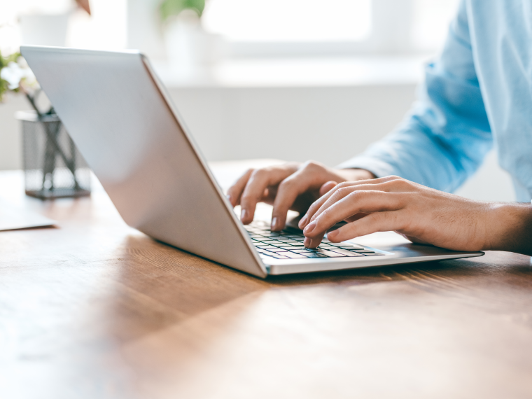 Handen typen op een laptop op een houten bureau, met een plant op de achtergrond
