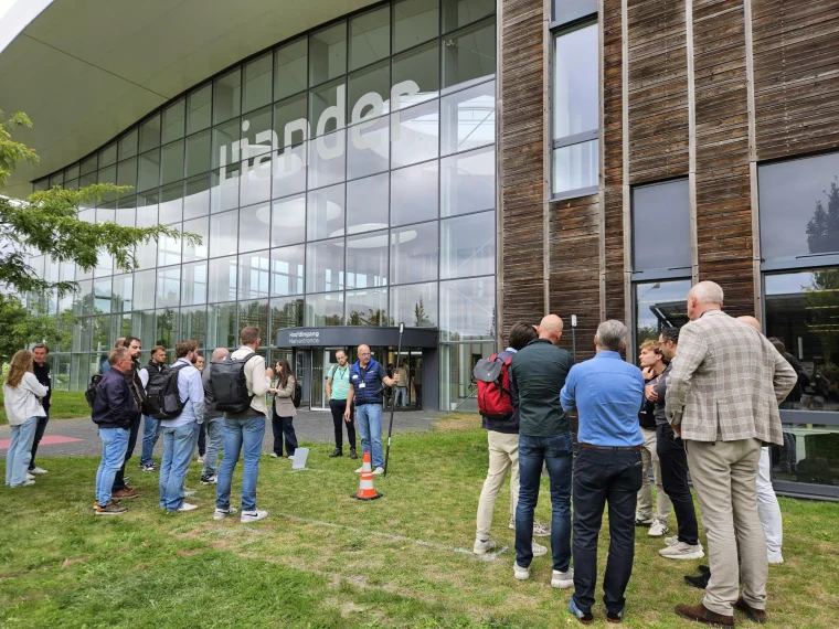 Deelnemers aan de Sectordag NLCS luisteren op het grasveld bij de hoofdingang van Liander naar uitleg bij een meetstok