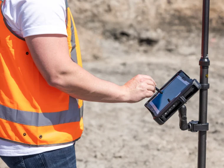 Medewerker in oranje hesje bedient met een stylus een robuuste tablet op een GNSS-meetstok
