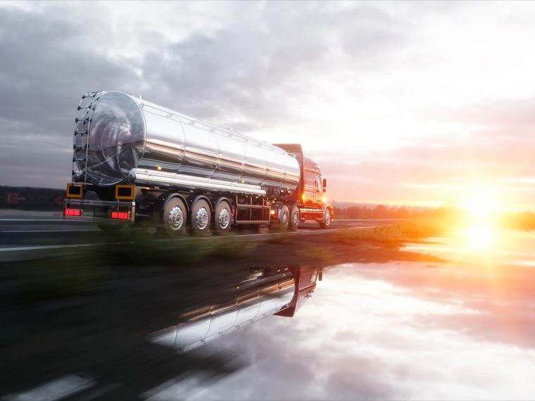 Tankwagen met glanzende tank rijdt over een natte weg bij zonsondergang