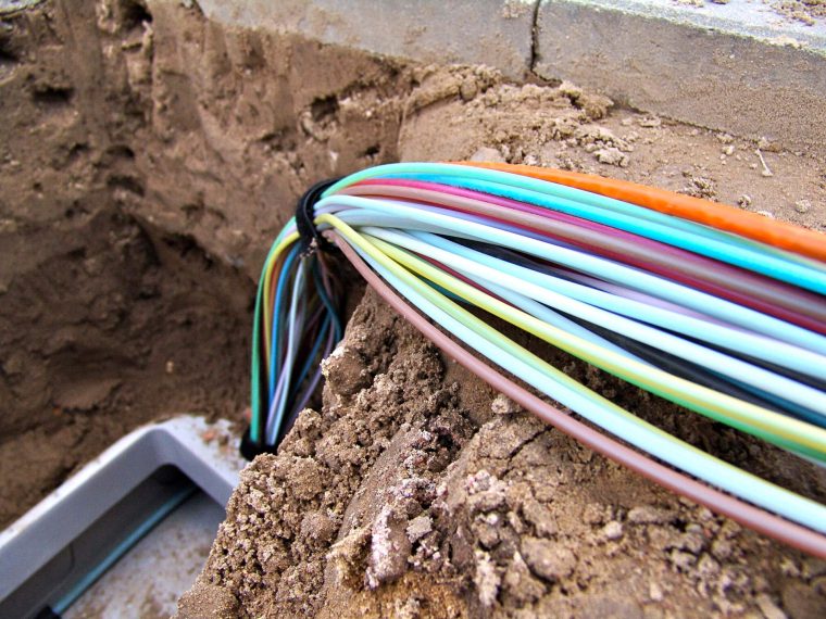 Bundel gekleurde kabels die uit het zand van een open sleuf steken, naast stoeptegels
