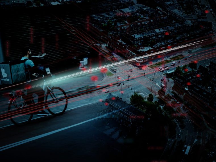 Fietskoerier op straat met daarachter een luchtfoto van een kruispunt, met rode lijnen en lichtpunten als datastromen