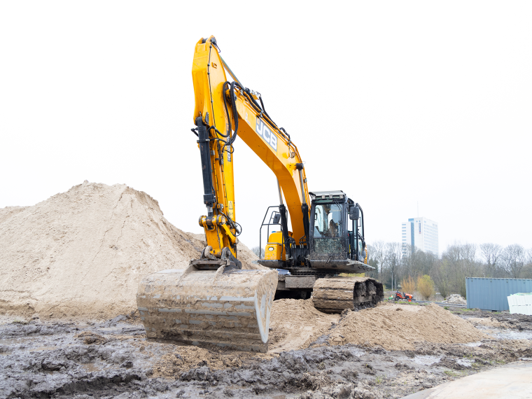 Gele graafmachine op een modderig bouwterrein naast een grote hoop zand